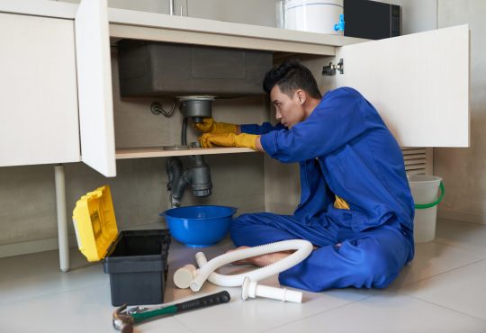 Young Vietnamese plumber checking drain in kitchen