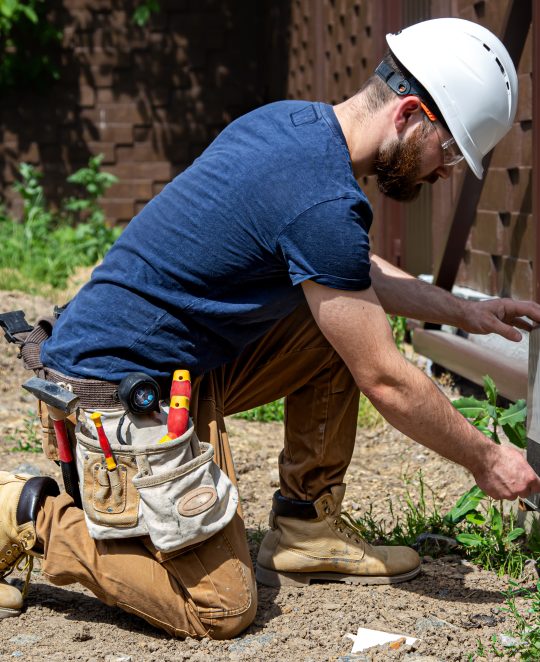 Electrician Builder at work, servicing the fuselage industrial switchboard. Professional in overalls with an electrician's tool.