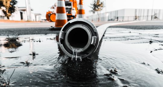 A selective closeup shot of a gray pipe with water coming out its hole